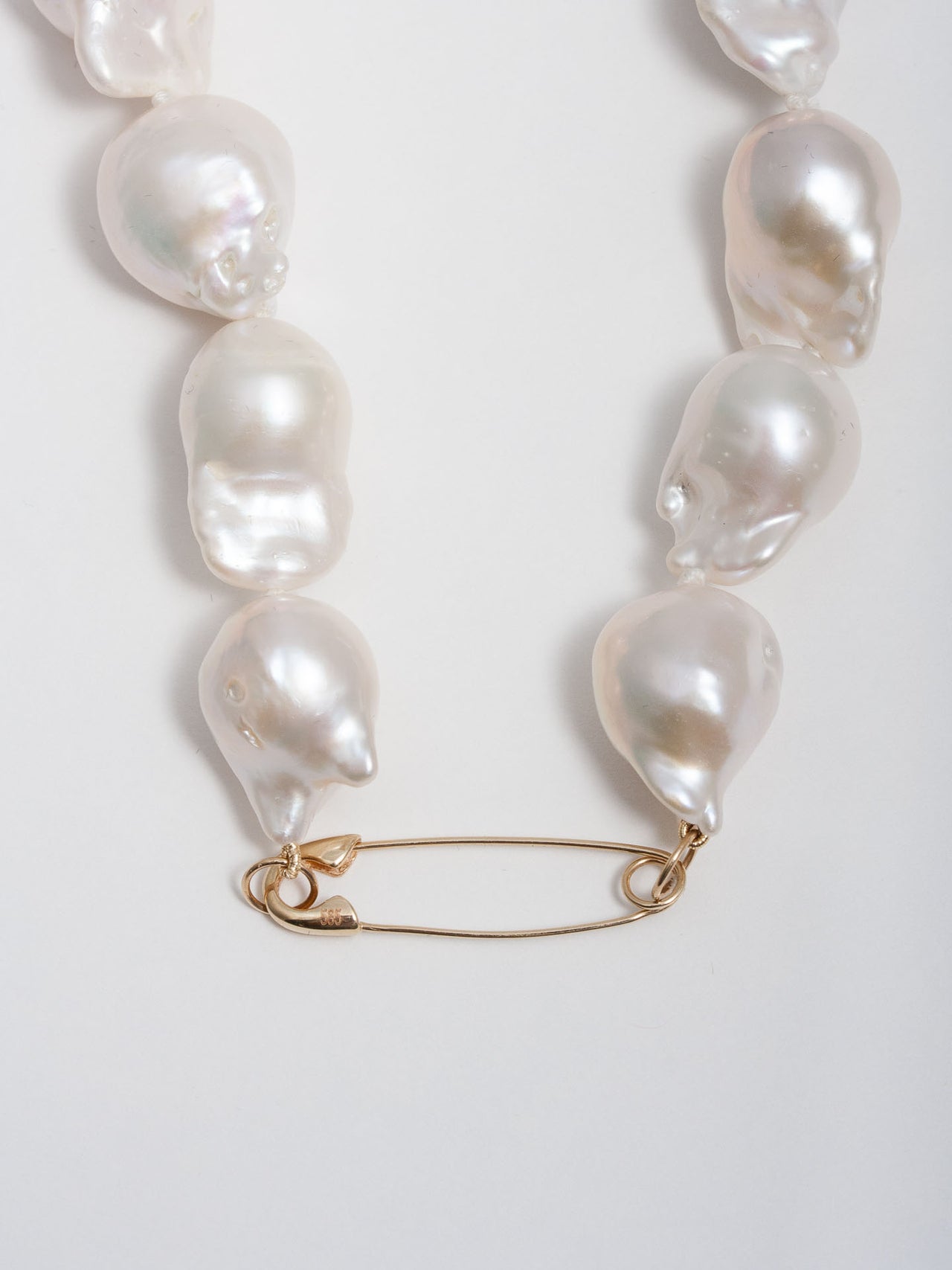 Close up of 14kt Yellow Gold Safety Pin Baroque Pearl Collar pictured on light grey background. 
