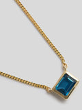 Close up of pendant on a product shot of Necklace with thin yellow gold chain and blue rectangle topaz pendant. Shot on white background.   