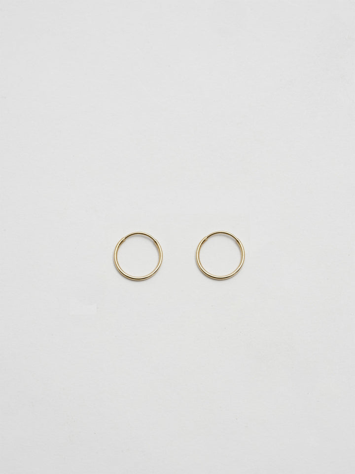 Product shot of the Valle Hoops (14Kt Yellow Gold Hoops 0.47” Diameter Thickness: 1mm) Background: Grey Backdrop