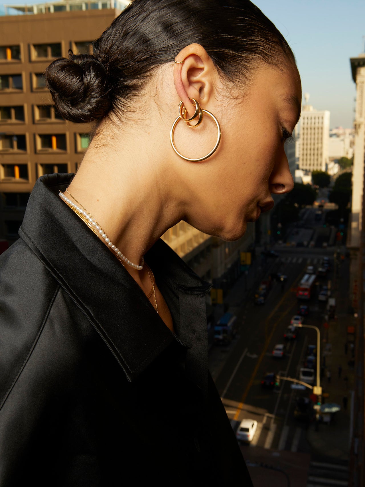 14kt Yellow Gold Midi Legacy Hoops pictured in models ear. City in background.