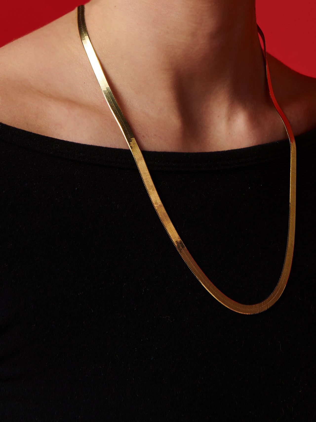Vermeil Ultra Herringbone Necklace pictured on models neck. Red background. 
