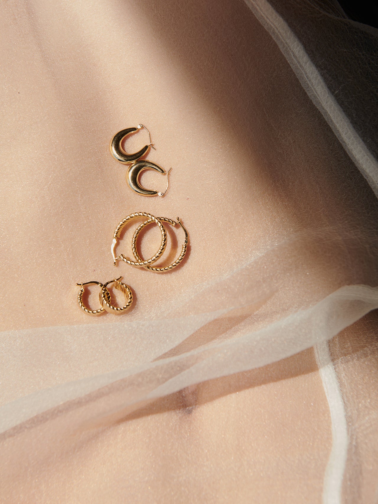 14kt Yellow Gold Dome Hammock Hoops pictured on stomach, silk material.