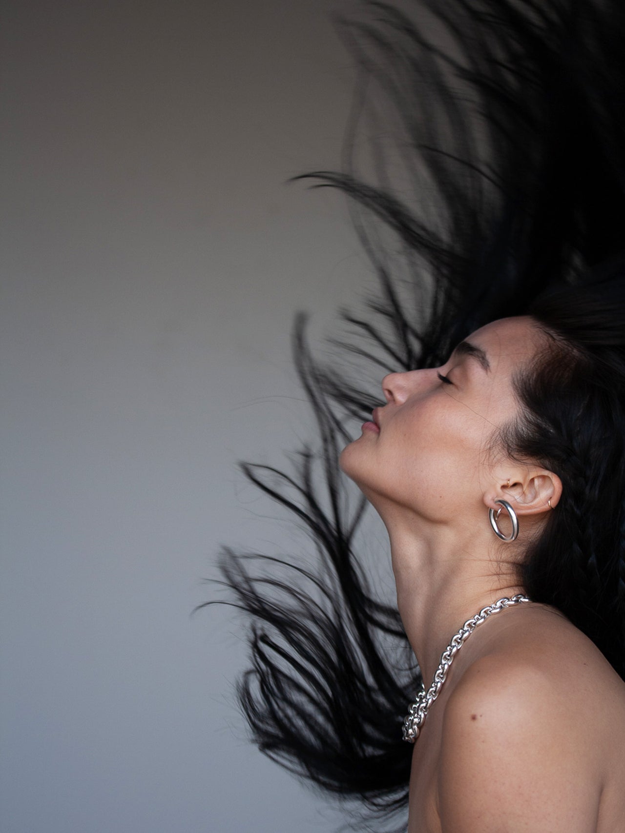 Creative shot of Euclid necklace on model. Flipping hair, light grey background. 