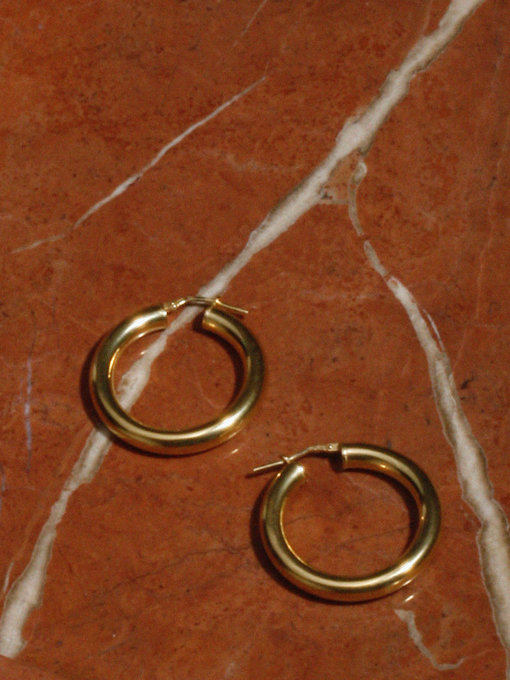 Close up of Vermeil Tube Hoops on marble tray. 