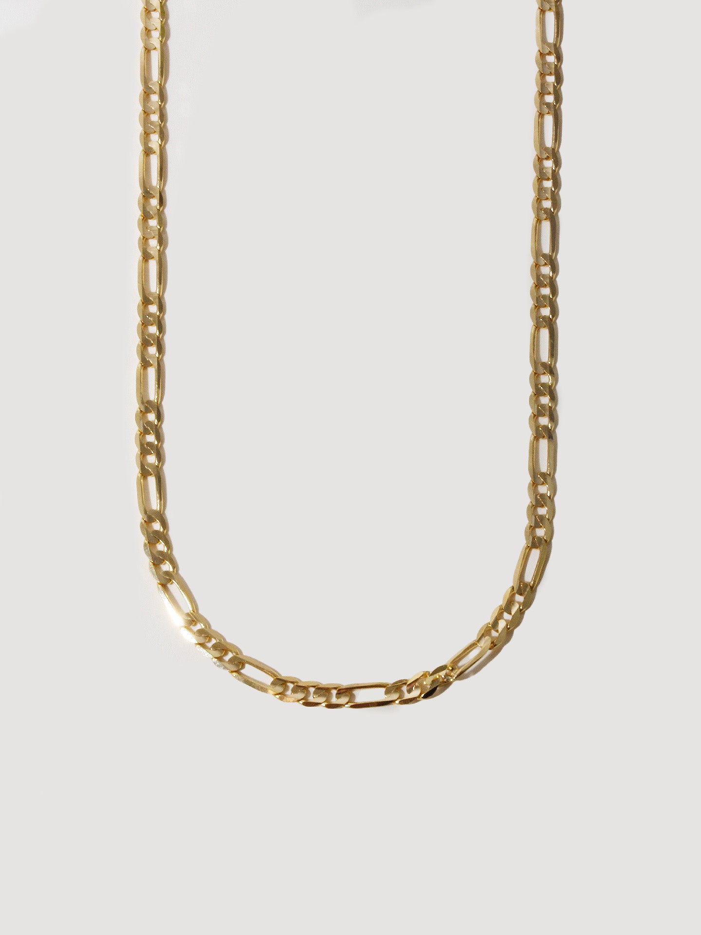 Close up of 14kt Yellow Gold Solid Figaro Chain Necklace pictured on light grey background.