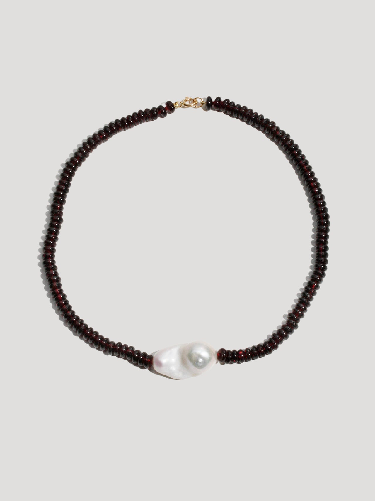 Necklace with dark beads and a pearl on a light gray background
