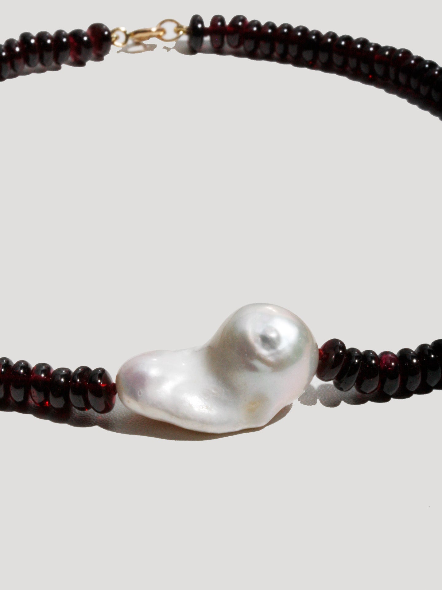Necklace with a large pearl pendant and dark bead chain on a light gray background