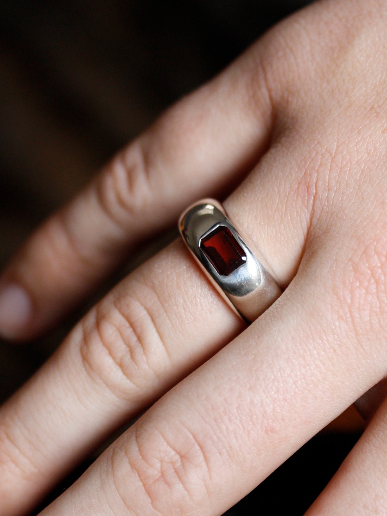 Silver ring with a red stone on a finger against a dark background
