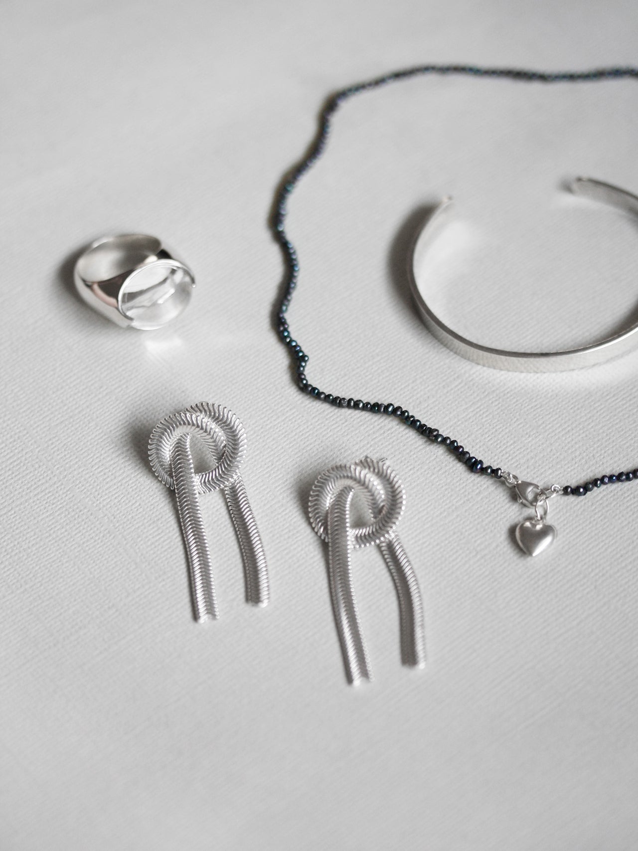 Silver jewelry set including earrings, necklace, and ring on a light gray background