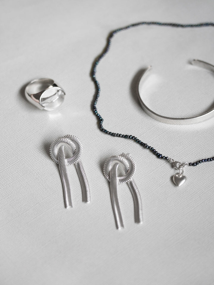 Silver jewelry set including earrings, necklace, and ring on a light gray background