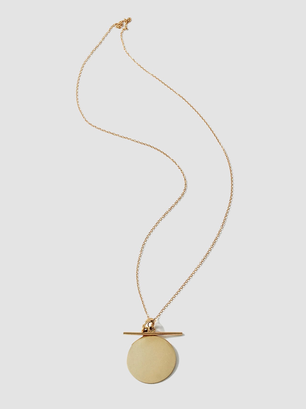 Gold necklace with a round pendant and toggle on a light gray background