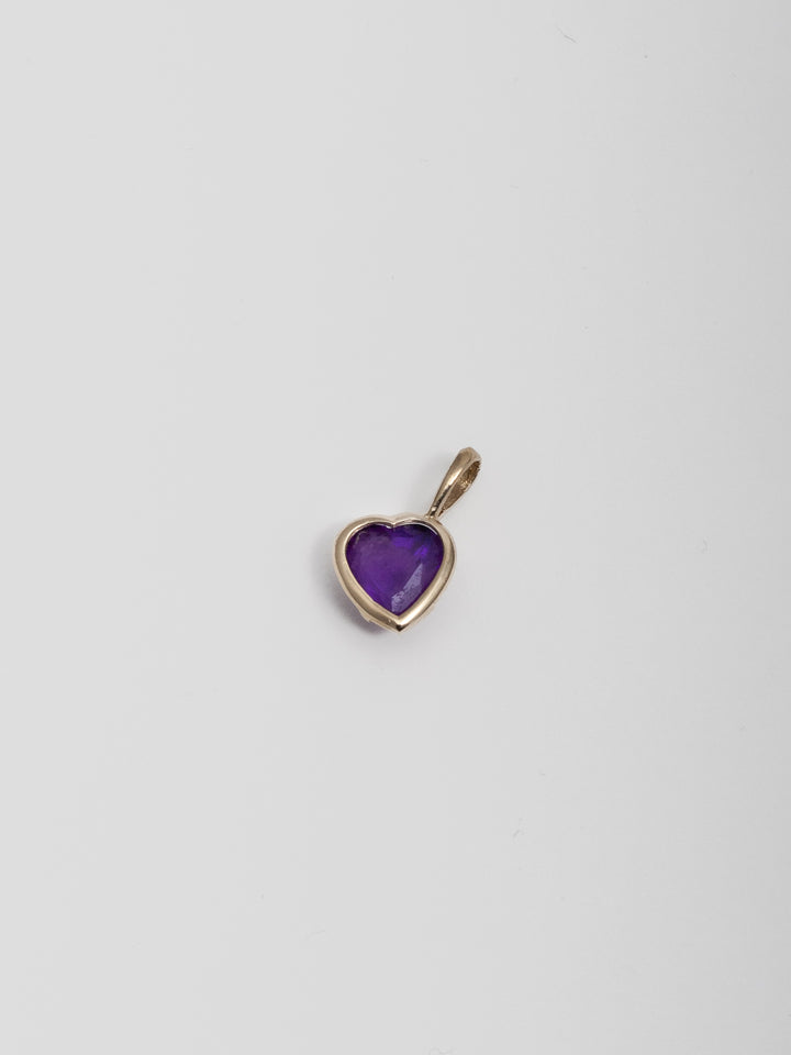 14kt Yellow Gold Amethyst Gemstone Heart Charm pictured on light grey background. 