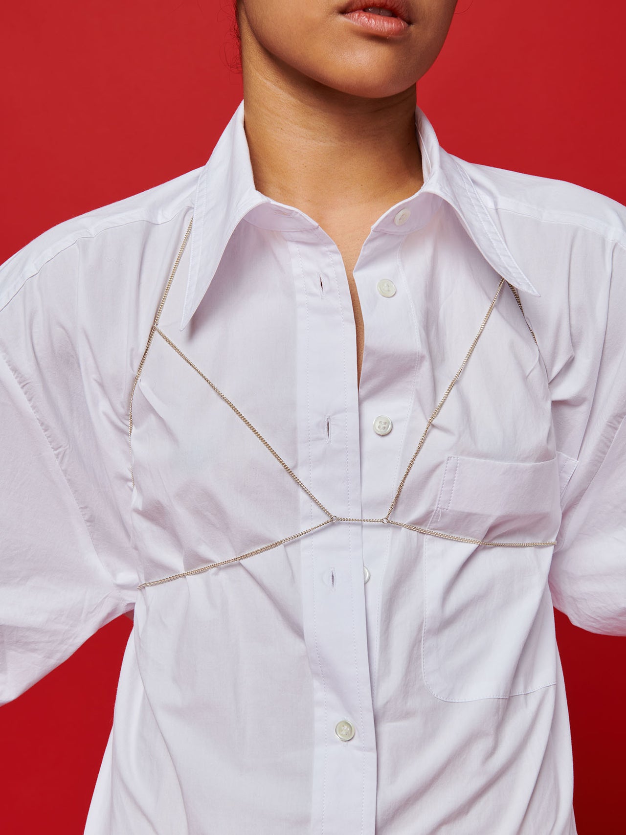 Sterling Silver Body Chain pictured on model worn over white button down. red background. close up.