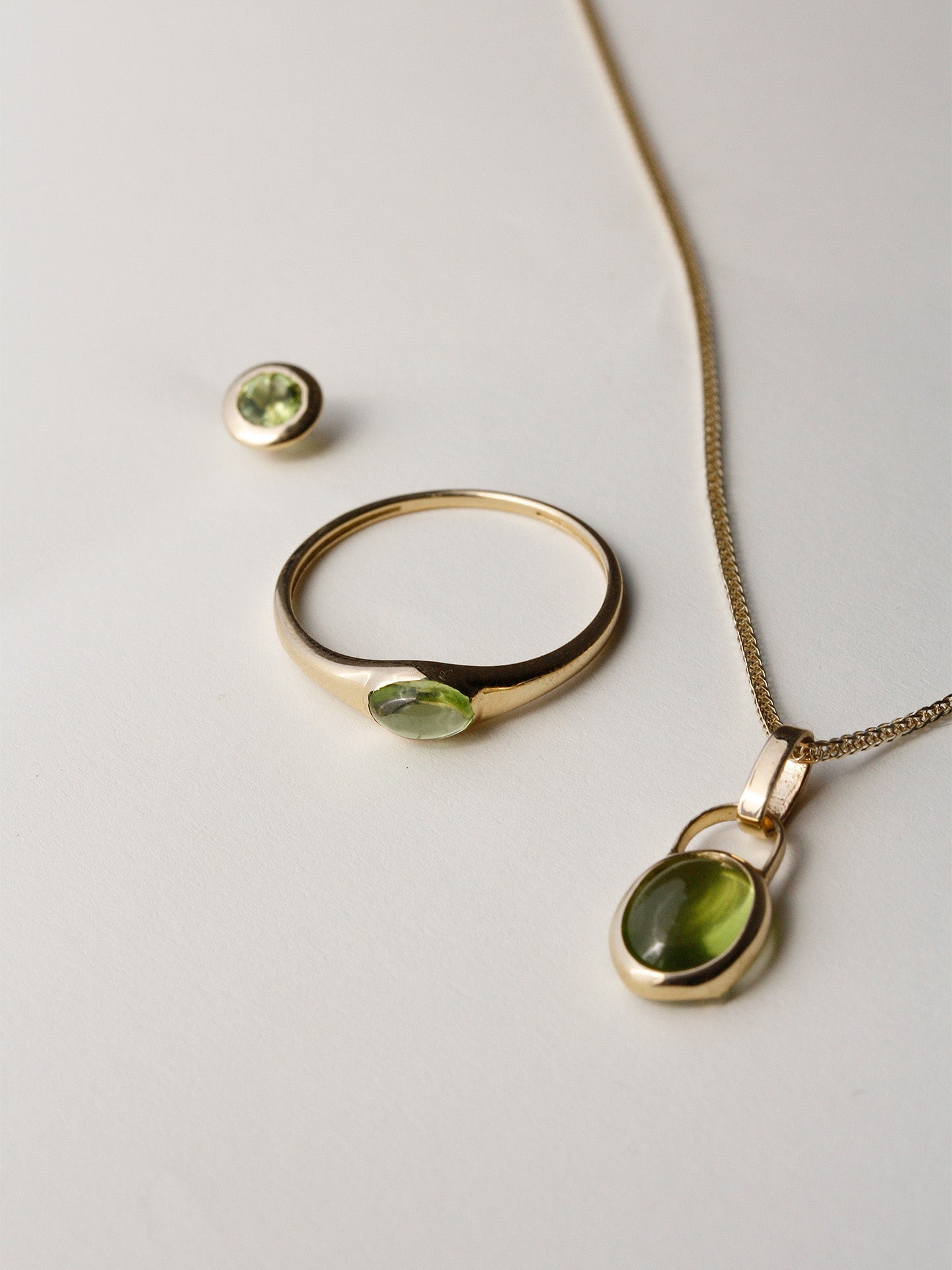Flat lay of Peridot Mini Gem Signet with the Padlock Charm Necklace and Peridot Bezel Stud on light grey background. 