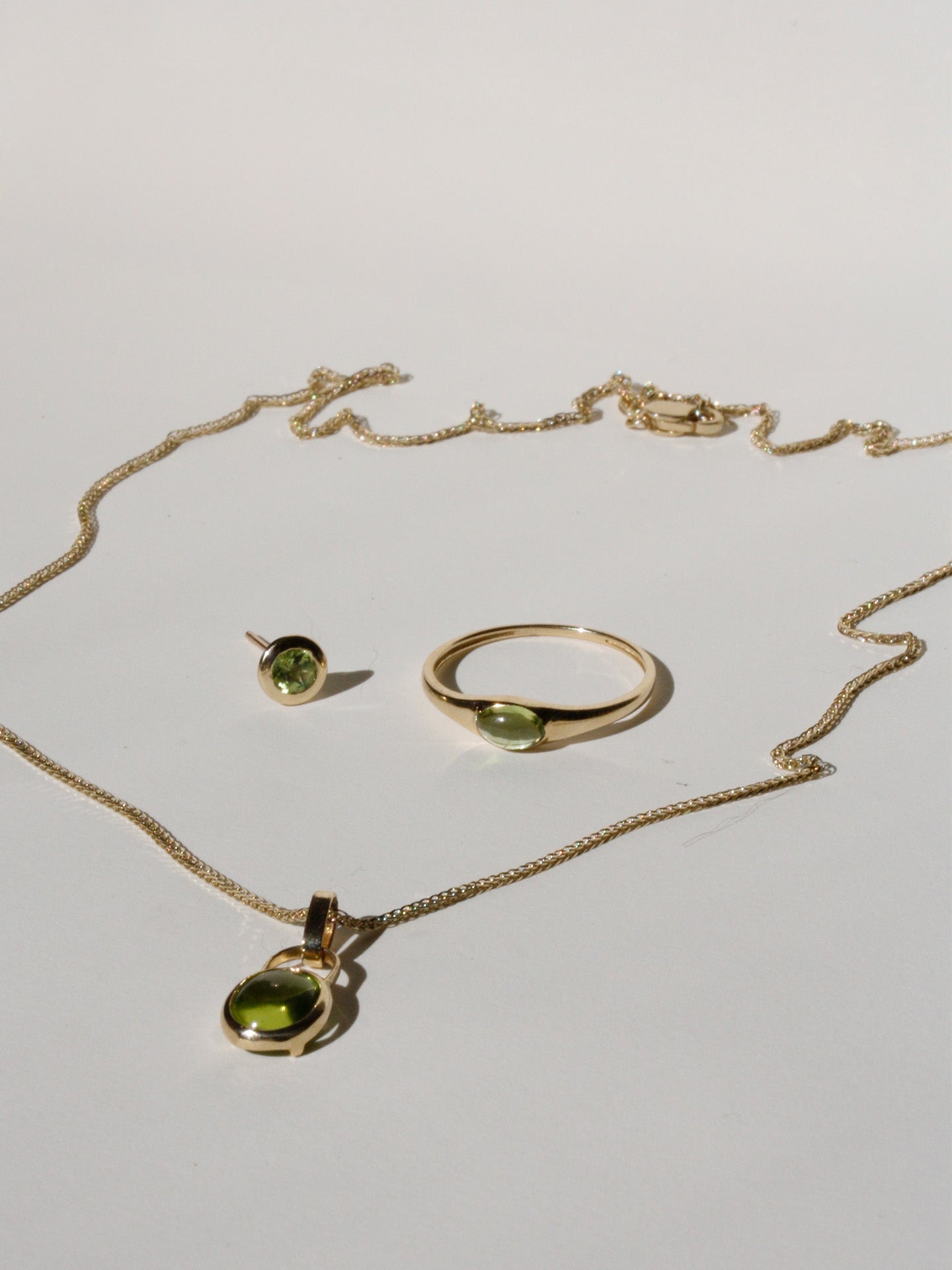 14kt Yellow Gold Peridot Bezel Stud pictured on light grey background with the Mini Gem Signet and Padlock Charm Necklace.
