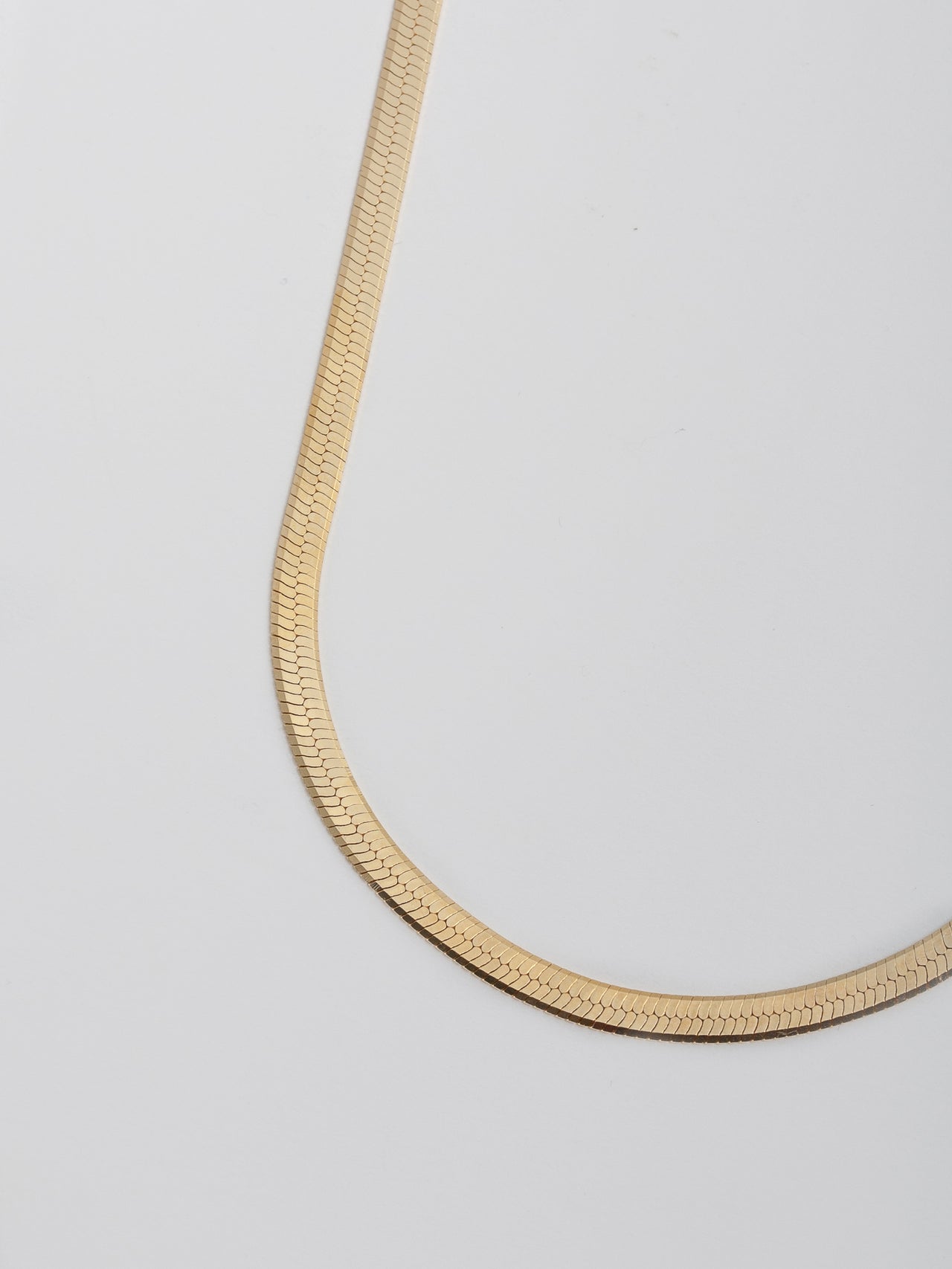 Vermeil Herringbone Chain Necklace pictured close up on light grey background.