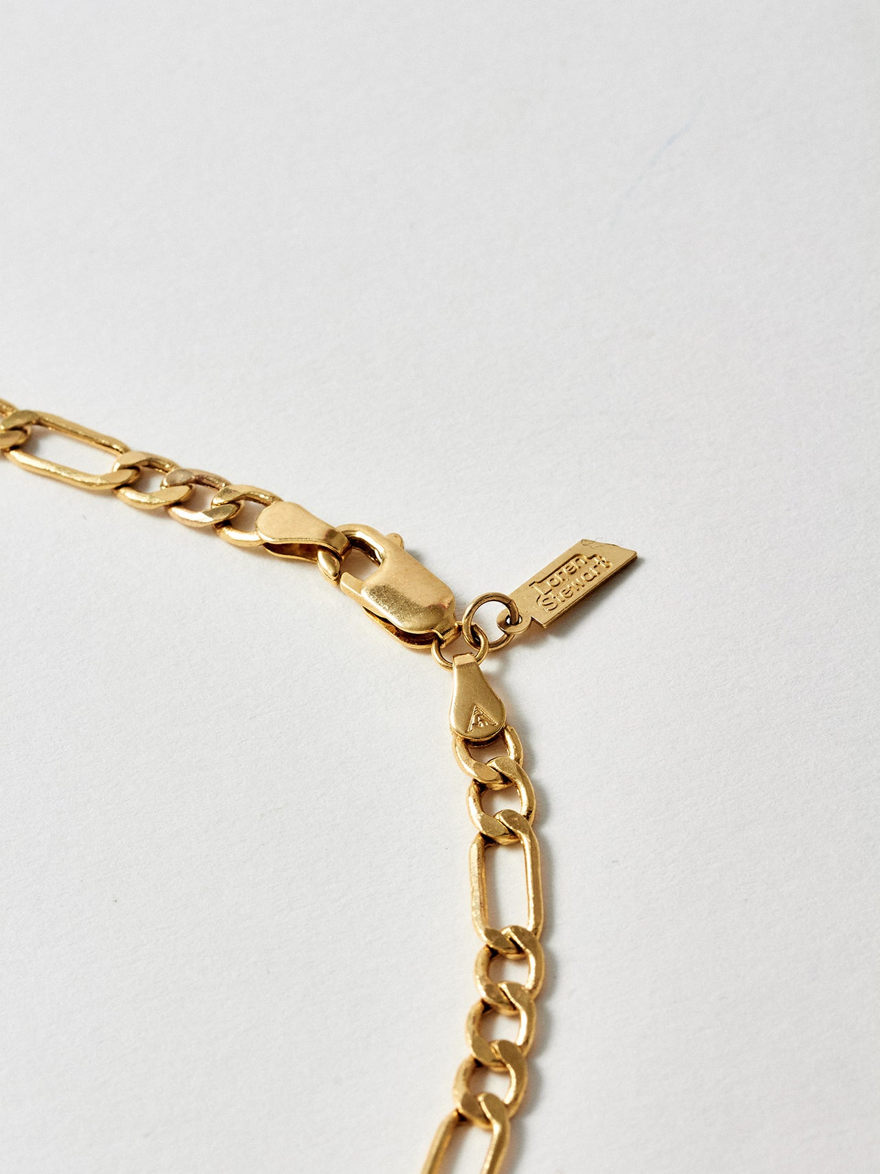 14Kt Yellow Gold Hollow Figaro Chain logo and lobster clasp closure pictured up close.