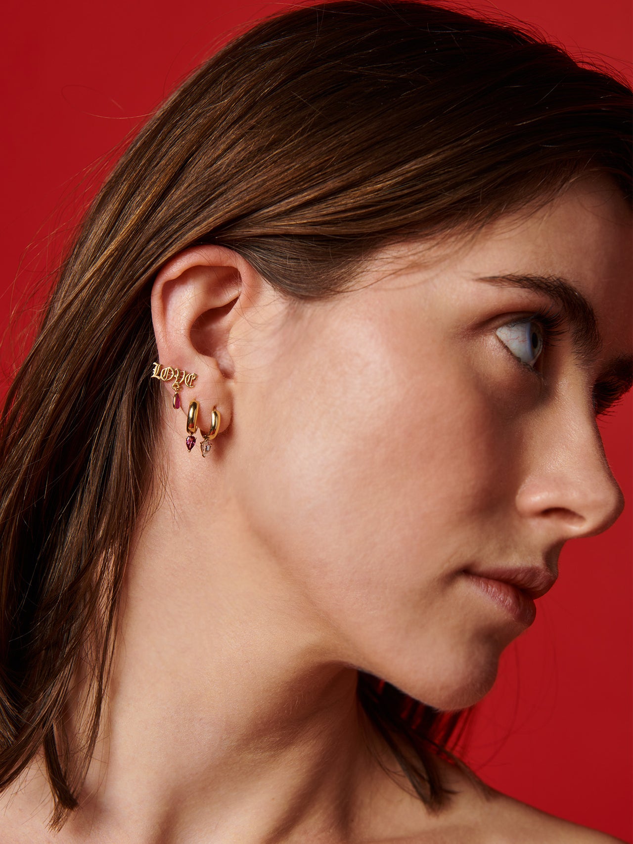 14kt Yellow Gold Gemstone Love Stud pictured on model. Red background.