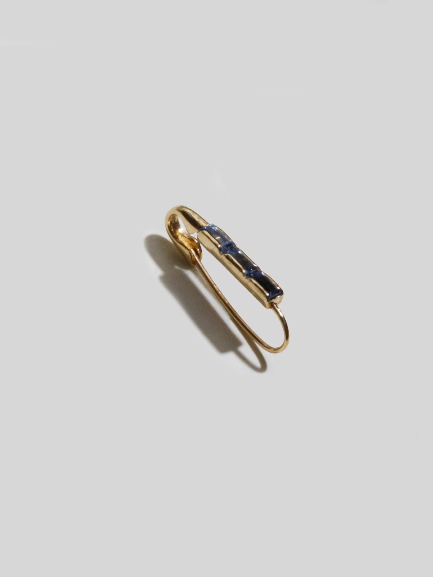 14kt Yellow Gold Mini Sapphire Baguette Safety Pin Earring pictured on light grey background. Slanted to see the side and front profile.