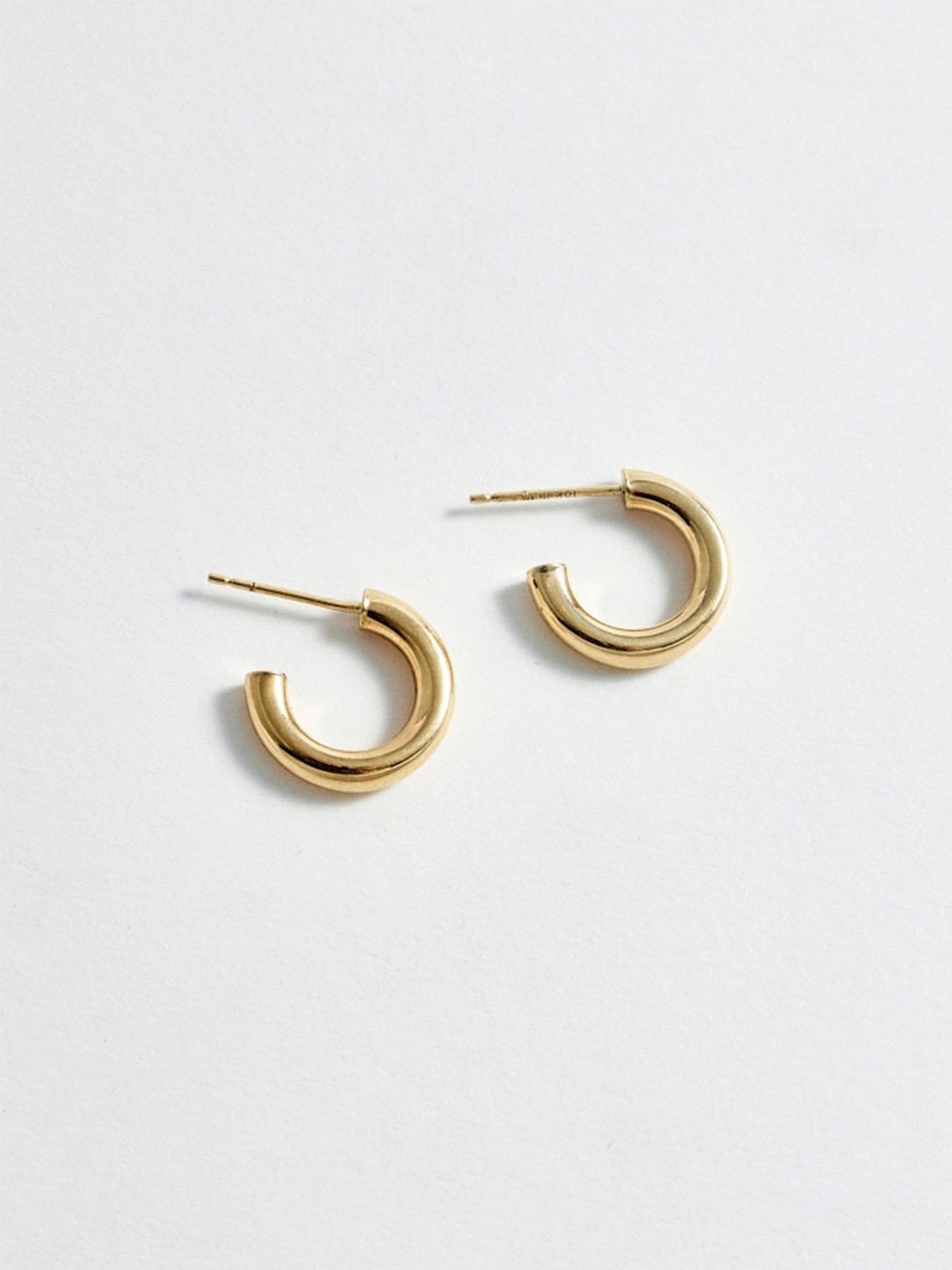 Product shot of the Chubbie Huggies (10Kt shinyYellow Gold Mini Tube Hoop Earrings Diameter: 16.51mm Thickness: 3mm) Background: Grey Backdrop