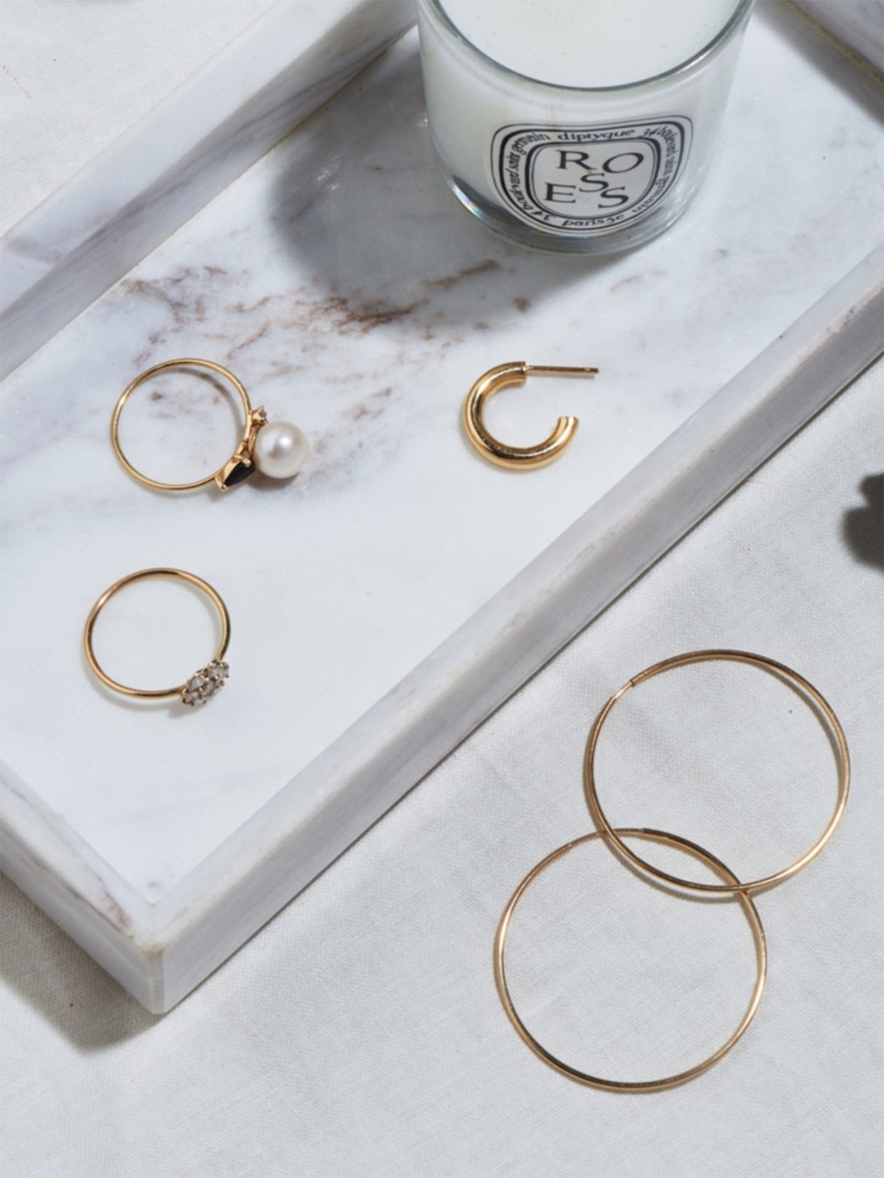Styled product shot of the Product shot of the Chubbie Huggies (10Kt shinyYellow Gold Mini Tube Hoop Earrings (Diameter: 16.51mm Thickness: 3mm) along with other gold products Background: Marble plate