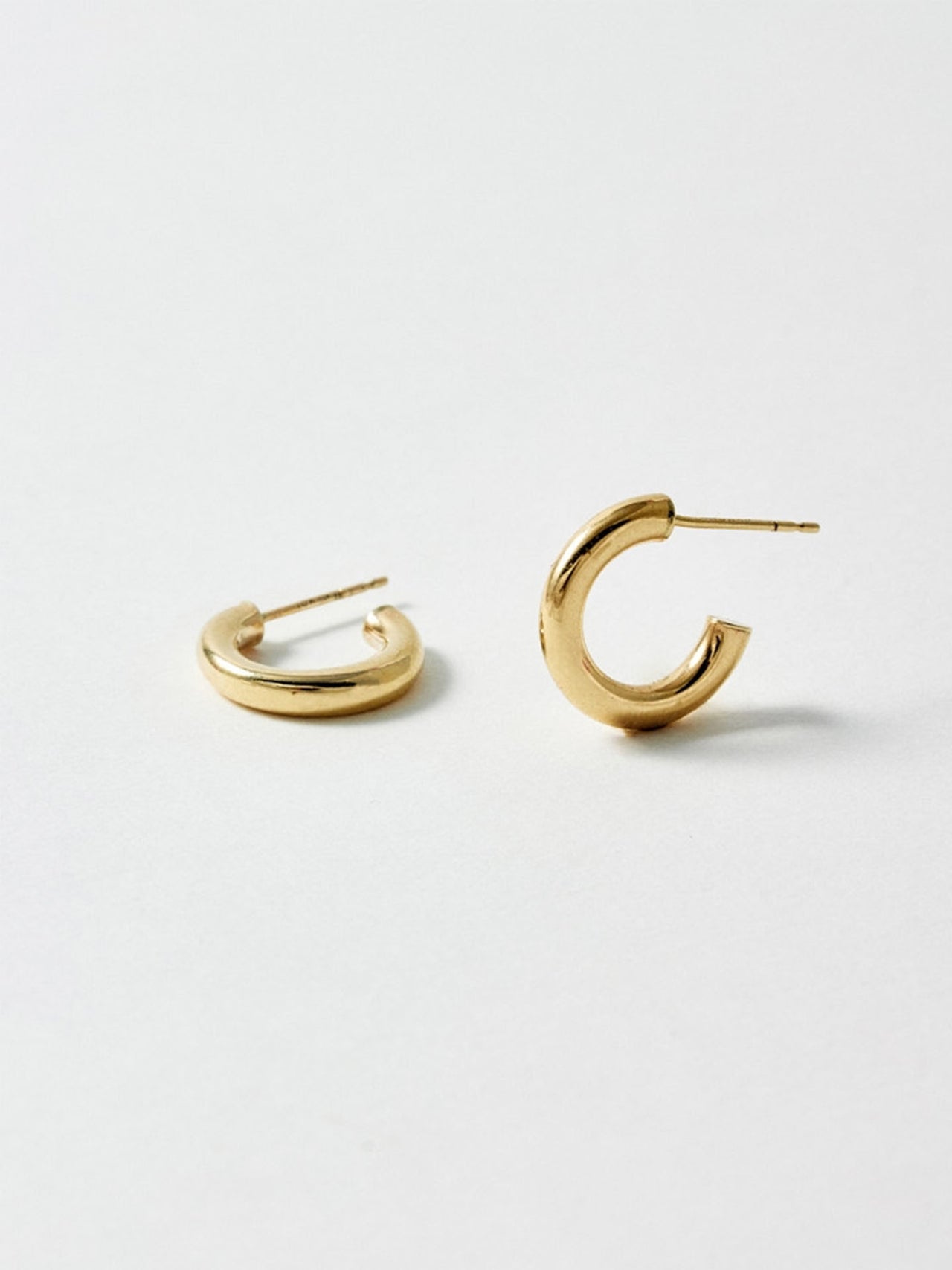 Styled product shot of the Chubbie Huggies (10Kt shinyYellow Gold Mini Tube Hoop Earrings Diameter: 16.51mm Thickness: 3mm) Background: Grey Backdrop