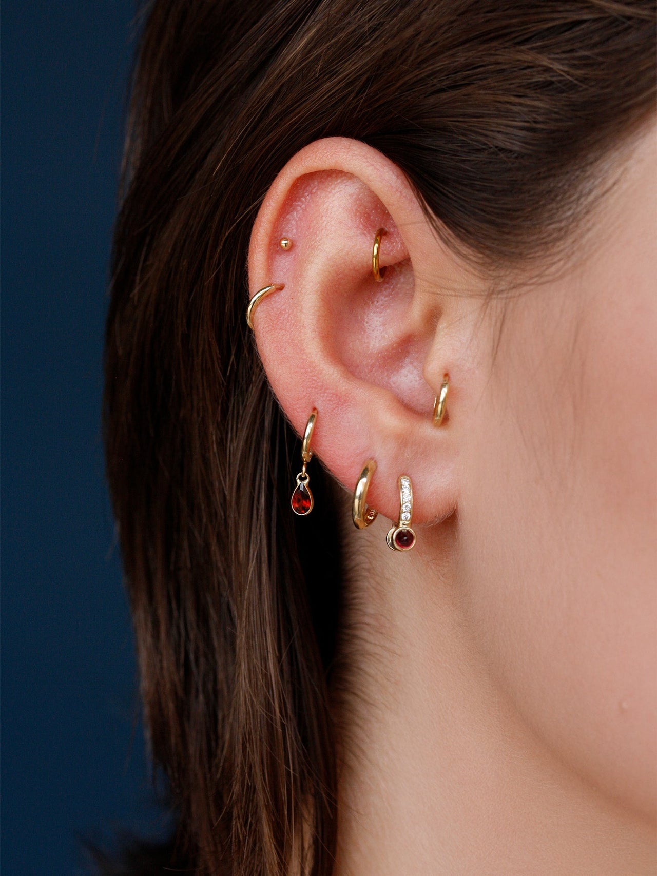 Close-up of an ear with multiple gold hoop earrings against a dark background