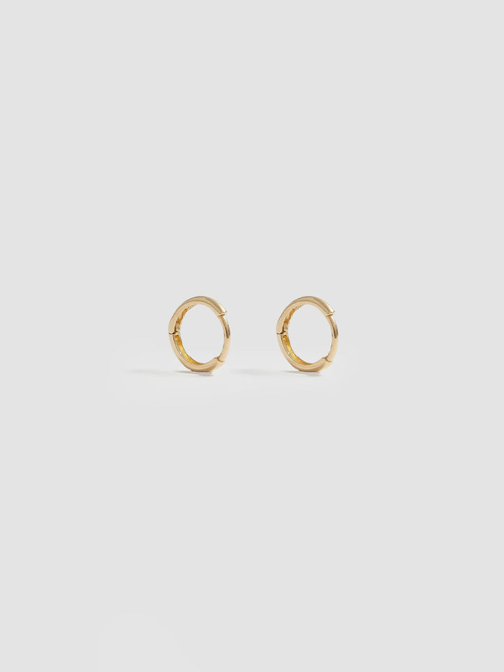 Product shot of the Elfin Mini Huggies (14KT Yellow Gold  8.6mm Diameter 1.4mm Thick) Background: Grey backdrop