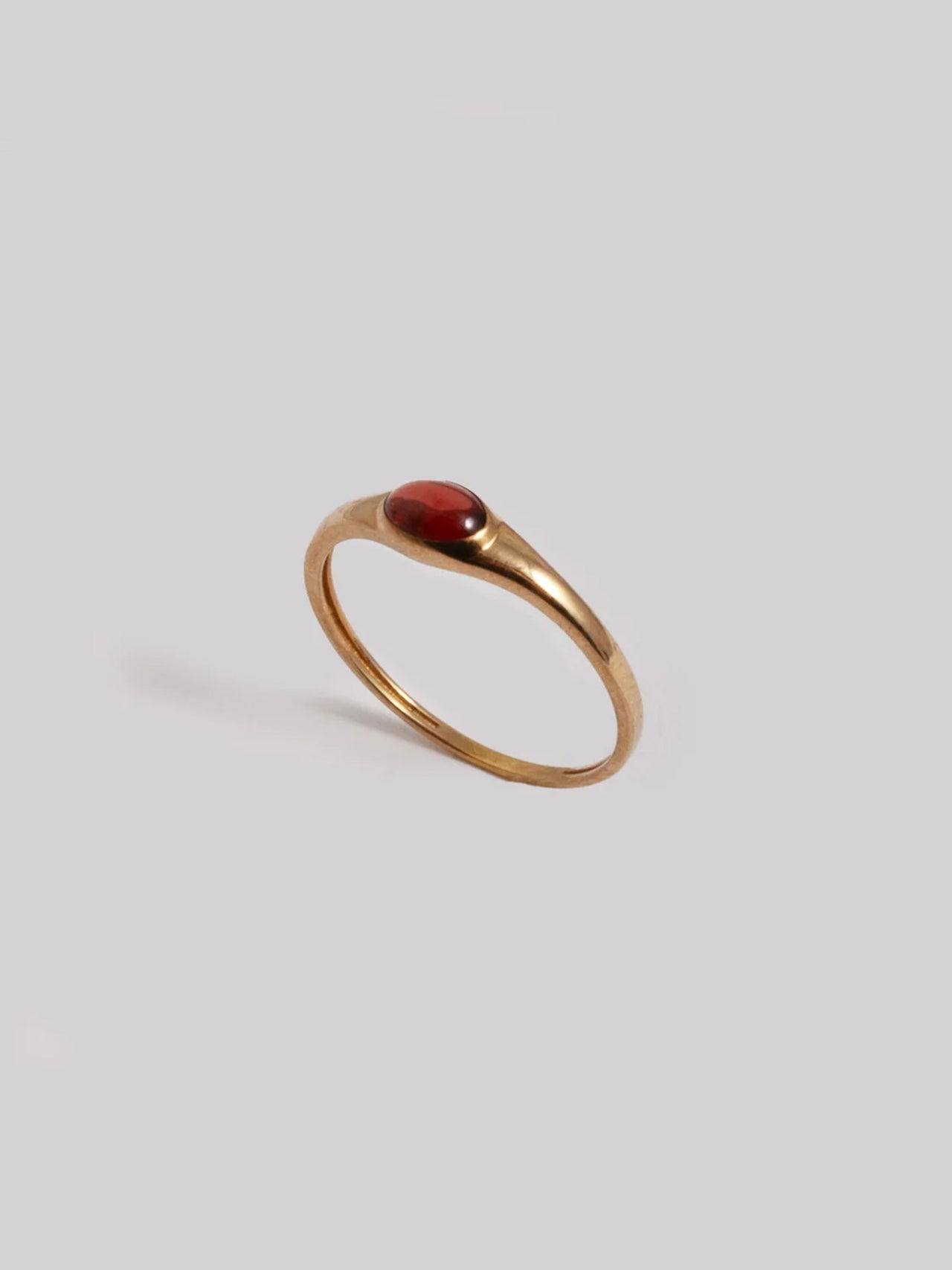 Gold ring with a red stone on a light gray background