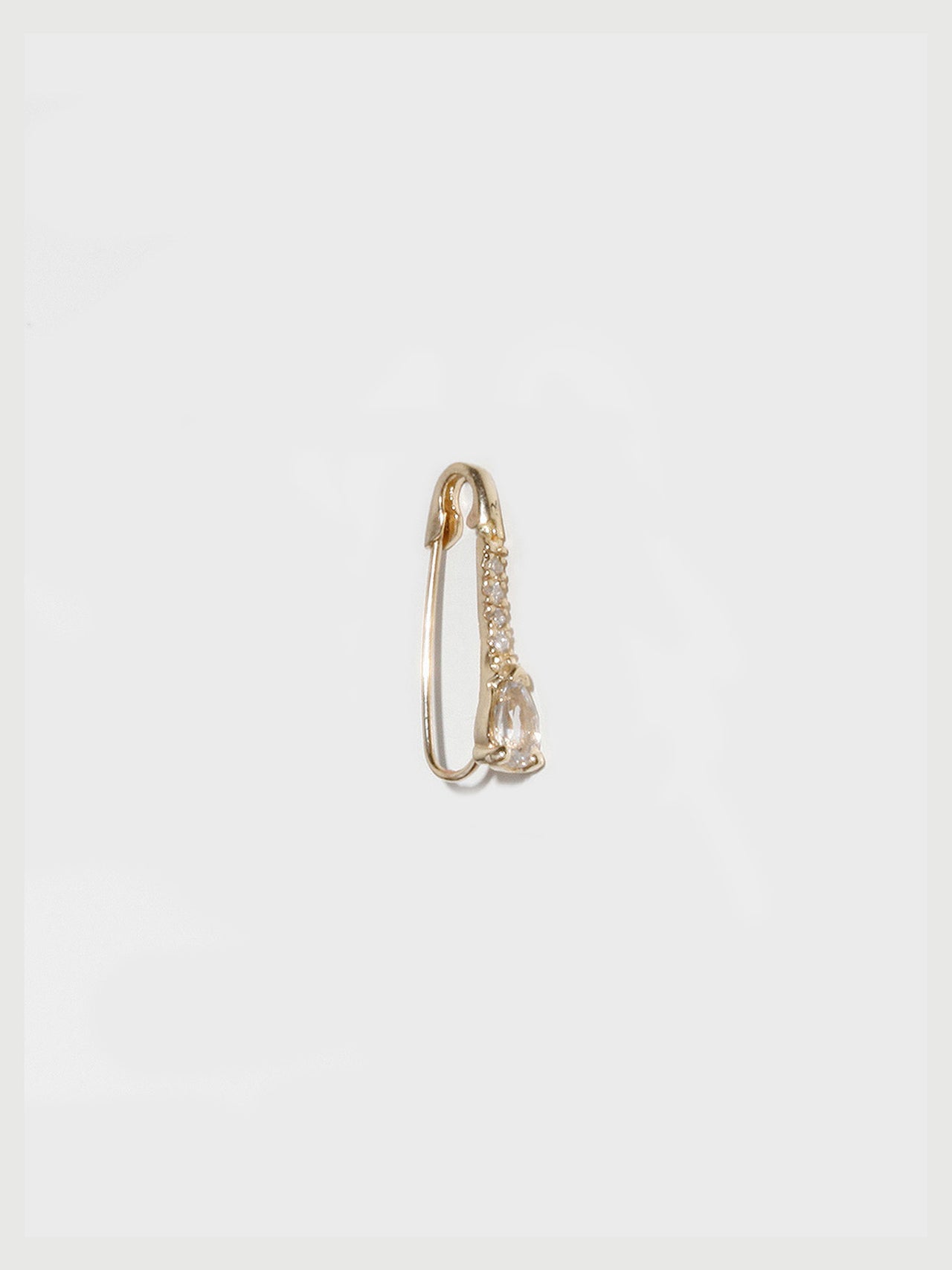 Gold safety pin earring on a light gray background