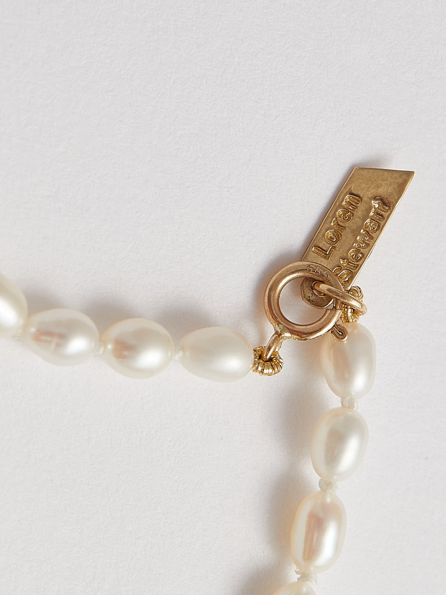 Product shot of White Rice Pearl Anklet including logo and closure. Light grey background.
