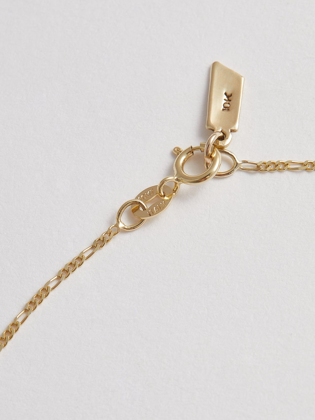 Close up product shot of the Baby Fig Chain Anklet closure (10kt Yellow Gold Figaro Chain Width: 1.3mm Thickness: 0.5mm Length: 10") Background: Grey backdrop