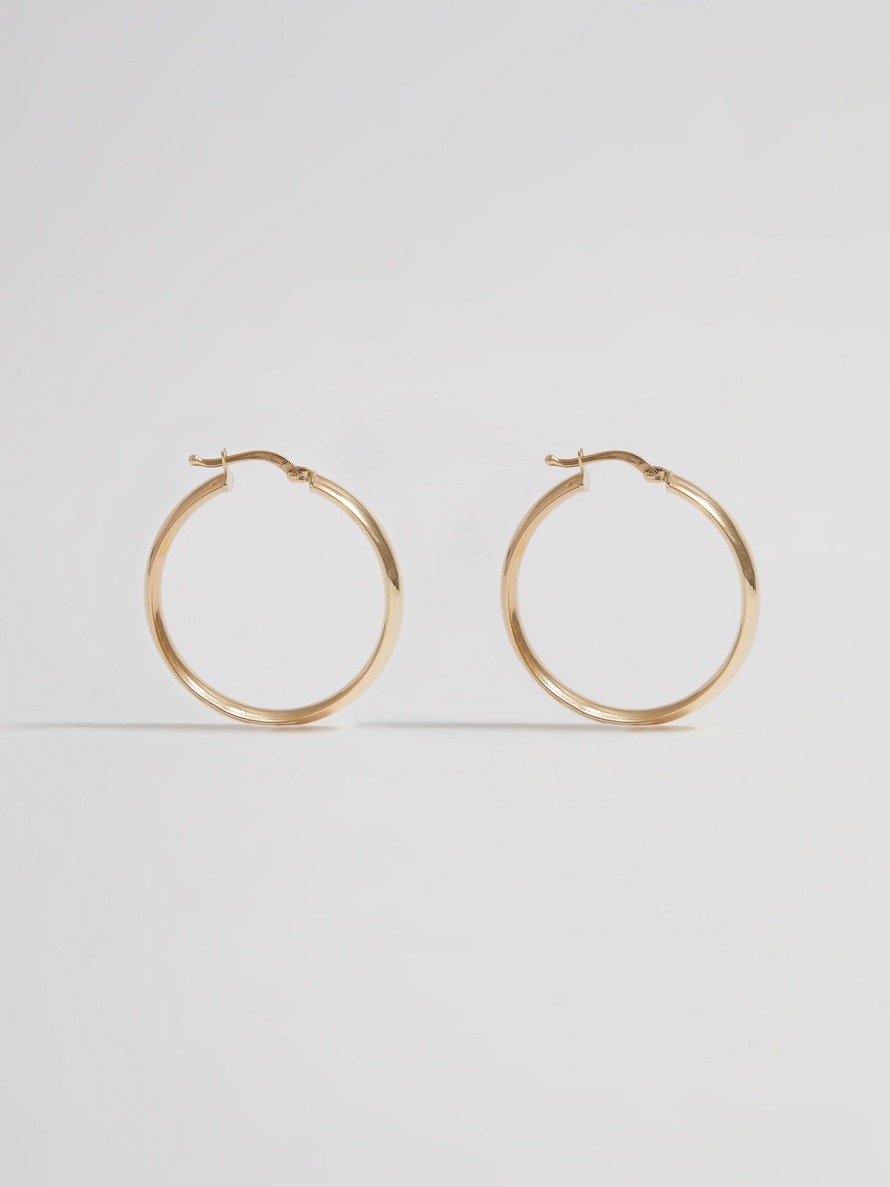 Product shot of the Legacy Hoops (14kt Yellow Gold 5mm Wide 30mm Diameter) Background: Grey backdrop