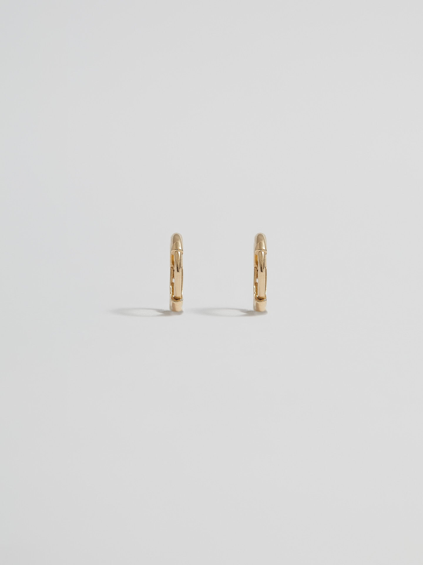 Product shot of the Elfin Mini Huggies (14KT Yellow Gold  8.6mm Diameter 1.4mm Thick) Background: Grey backdrop