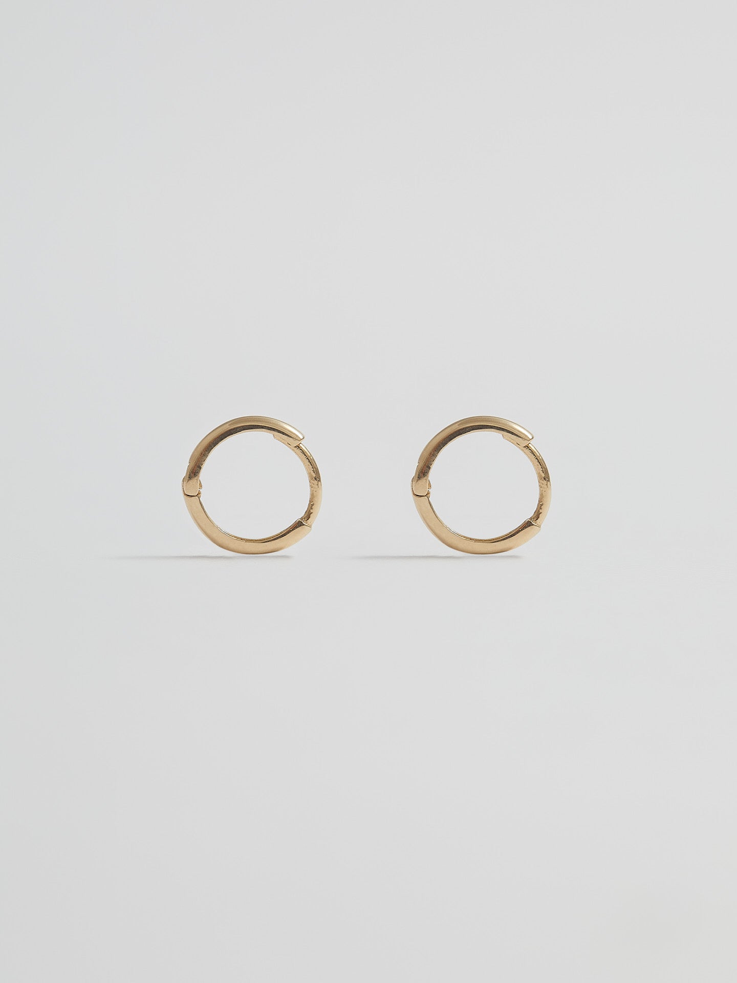 Product shot of the Elfin Mini Huggies (14KT Yellow Gold  8.6mm Diameter 1.4mm Thick) Background: Grey backdrop