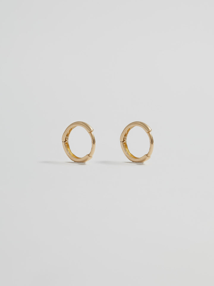 Product shot of the Elfin Mini Huggies (14KT Yellow Gold  8.6mm Diameter 1.4mm Thick) Background: Grey backdrop