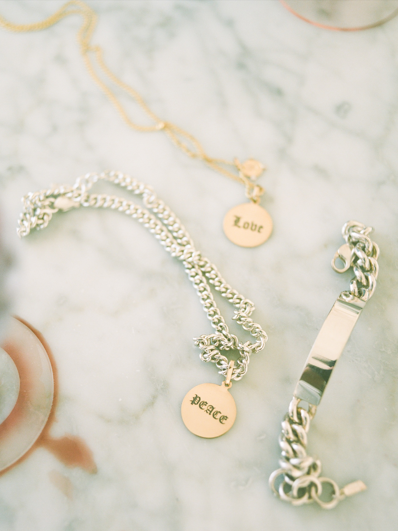 flat lay imagery of disk pendants engraved with the words "love" and "peace" in gothic writing on marble backdrop