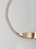 Close up of the Mini Ellipse Bracelet on light grey background. Sterling Silver Curb Chain with 14kt Yellow Gold Oval ID.