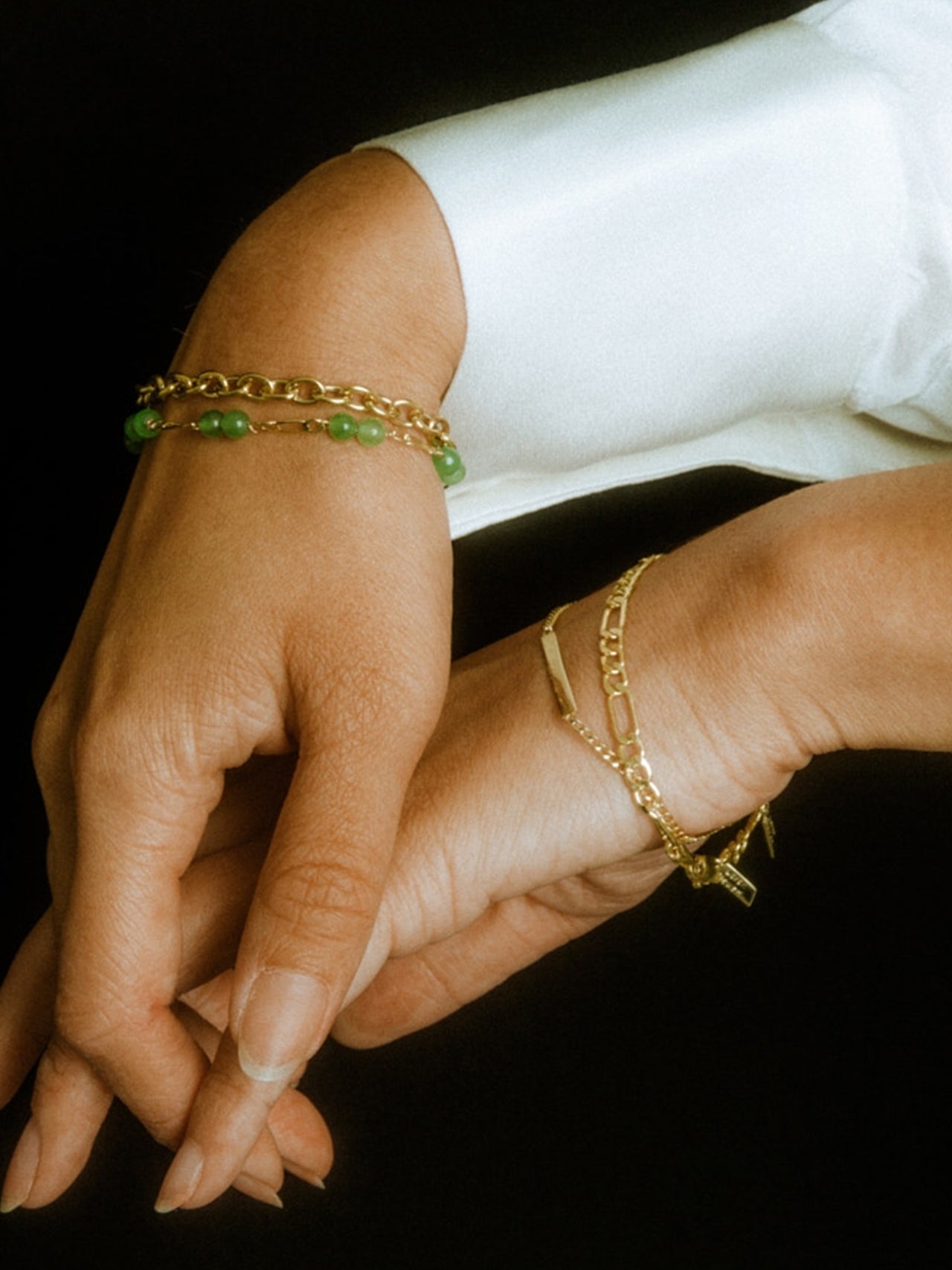 Yellow Gold XL Figaro Chain Bracelet pictured on models wrist along with three other bracelets pictured in frame. Black background. 