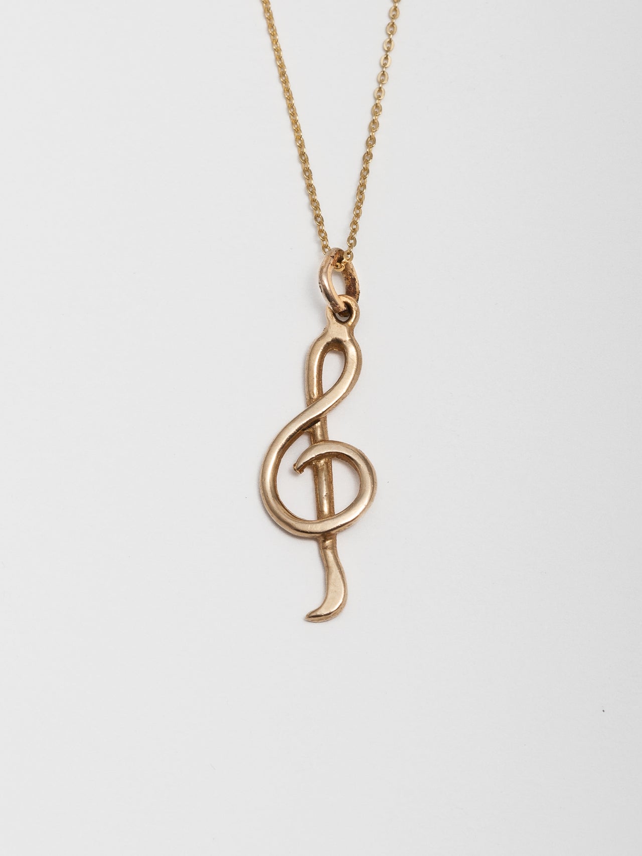 Close up of 14Kt Yellow Gold Music Note Pendant pictured on light grey background. 