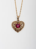 Close up picture of 14Kt Yellow Gold Heart Pendant with CZ Ruby Heart pictured on chain. Light grey background. 