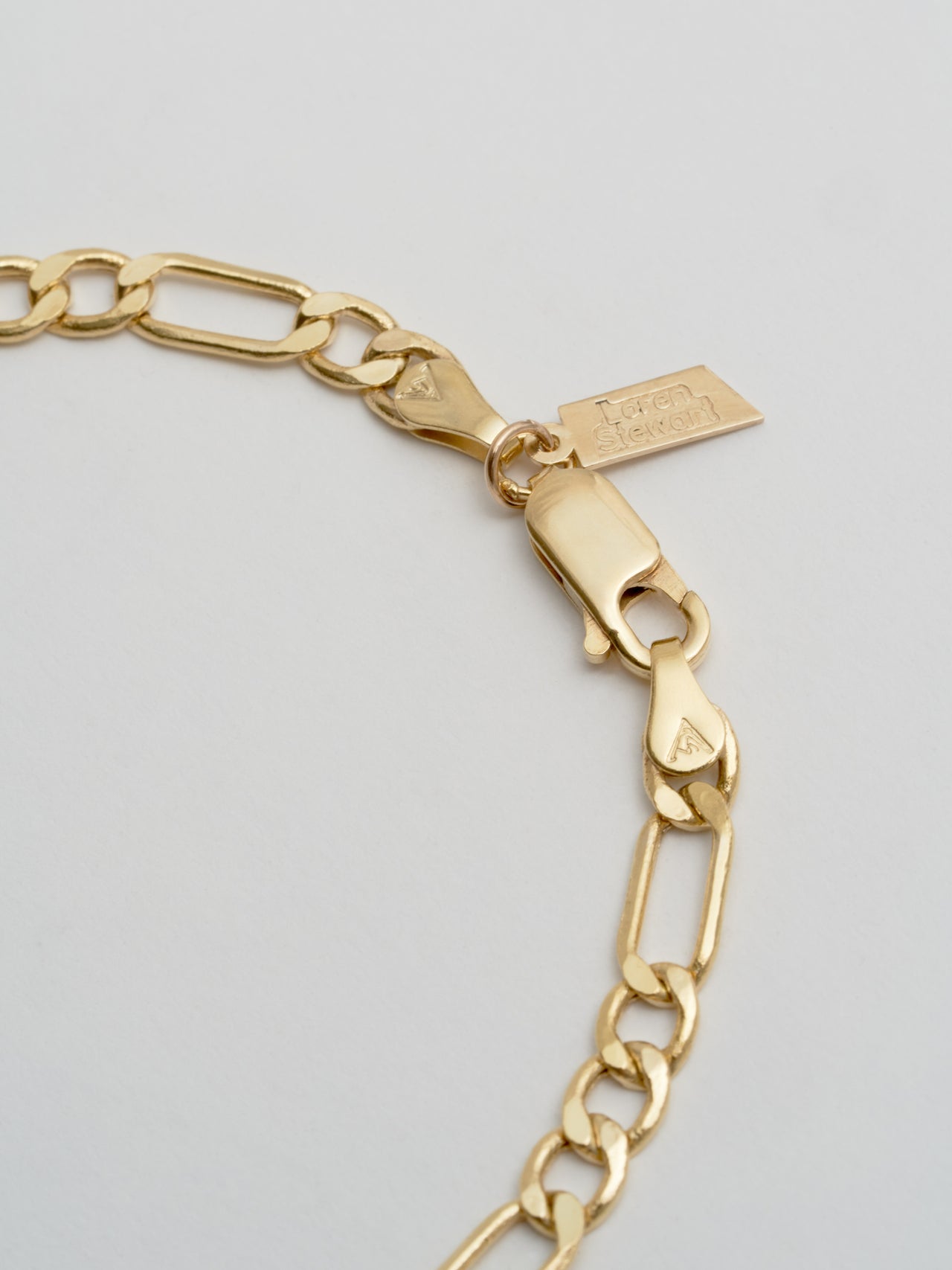 Up close view of the Yellow Gold XL Figaro Chain bracelet. Pictures lobster clasp and rectangle Loren Stewart logo. 
