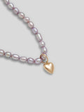Close up of yellow gold heart pendant on lavender pearl necklace. 