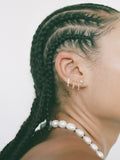 yellow gold bolla hoops shot on models ear. Stacked with other earrings. Light grey background. 