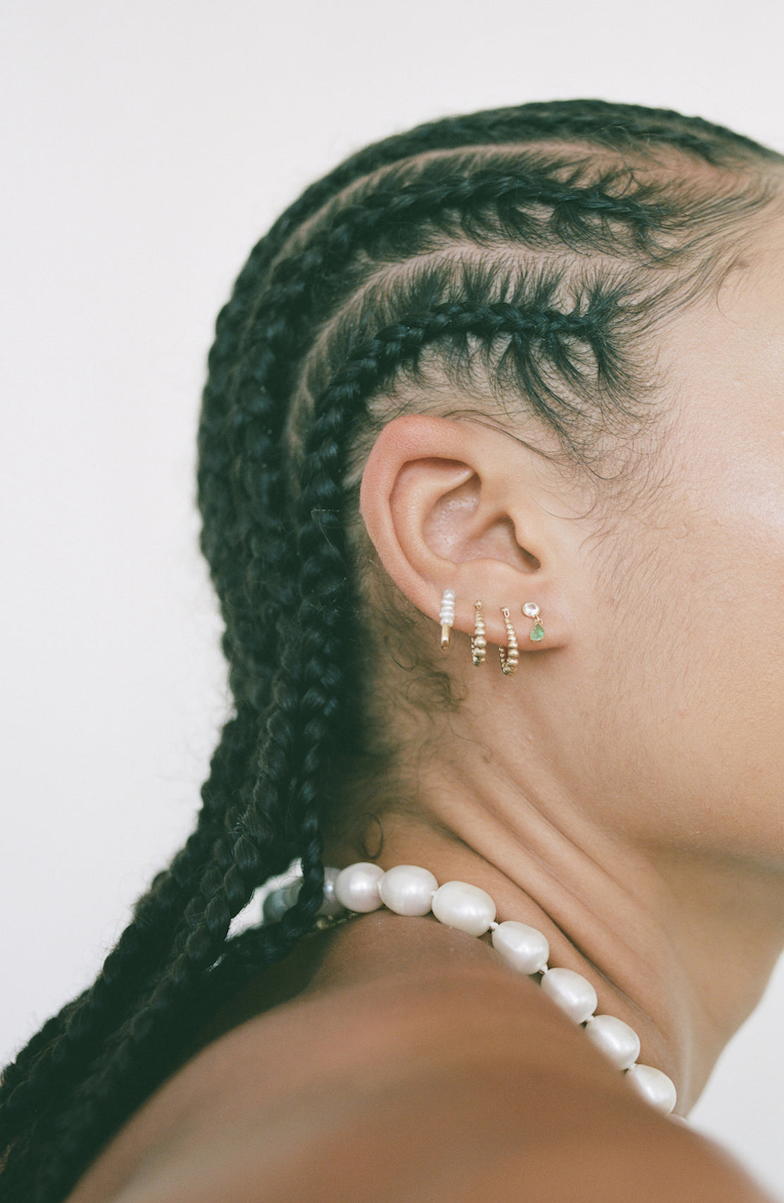yellow gold bolla hoops shot on models ear. Stacked with other earrings. Light grey background. 