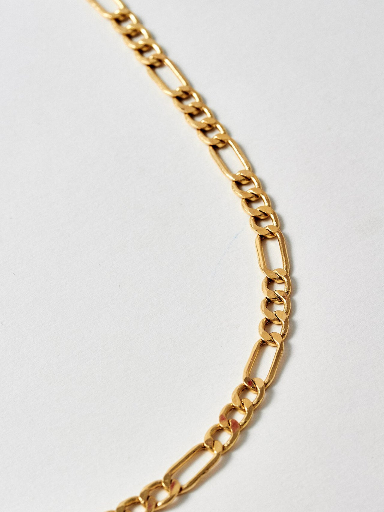 Close up shot of 14KT Yellow Gold Figaro Chain. Shot on light grey background. 