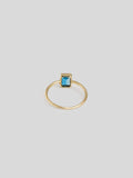 VERITCAL BLUE TOPAZ GEM ENCASED IN GOLD ON THIN YELLOW GOOD RING BAND. SHOT WITH WHITE BACKGROUND