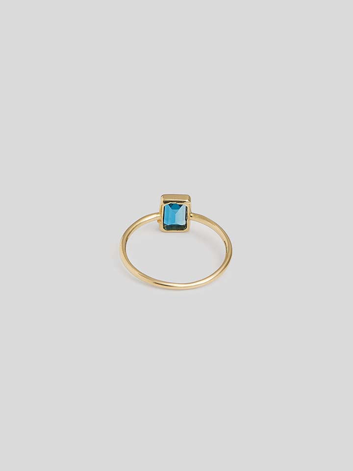 VERITCAL BLUE TOPAZ GEM ENCASED IN GOLD ON THIN YELLOW GOOD RING BAND. SHOT WITH WHITE BACKGROUND