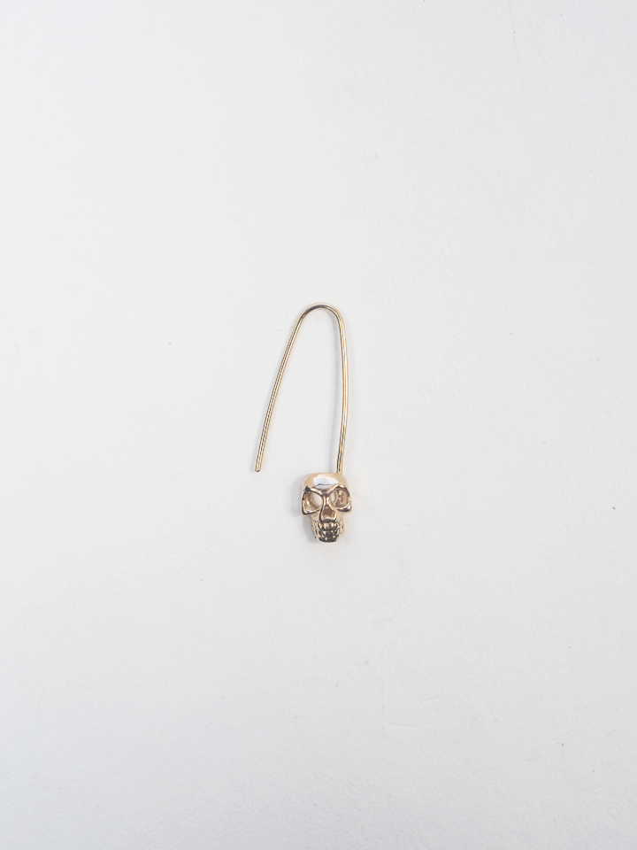 Product image of yellow gold safety pin with skull at base of pin, shot on white background. 