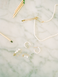 Flat lay of mini mixed pearl safety pin earring on marble backdrop with other pearl styles